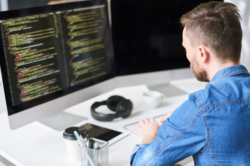 Programador sentado de espaldas mientras escribe el código de una aplicación